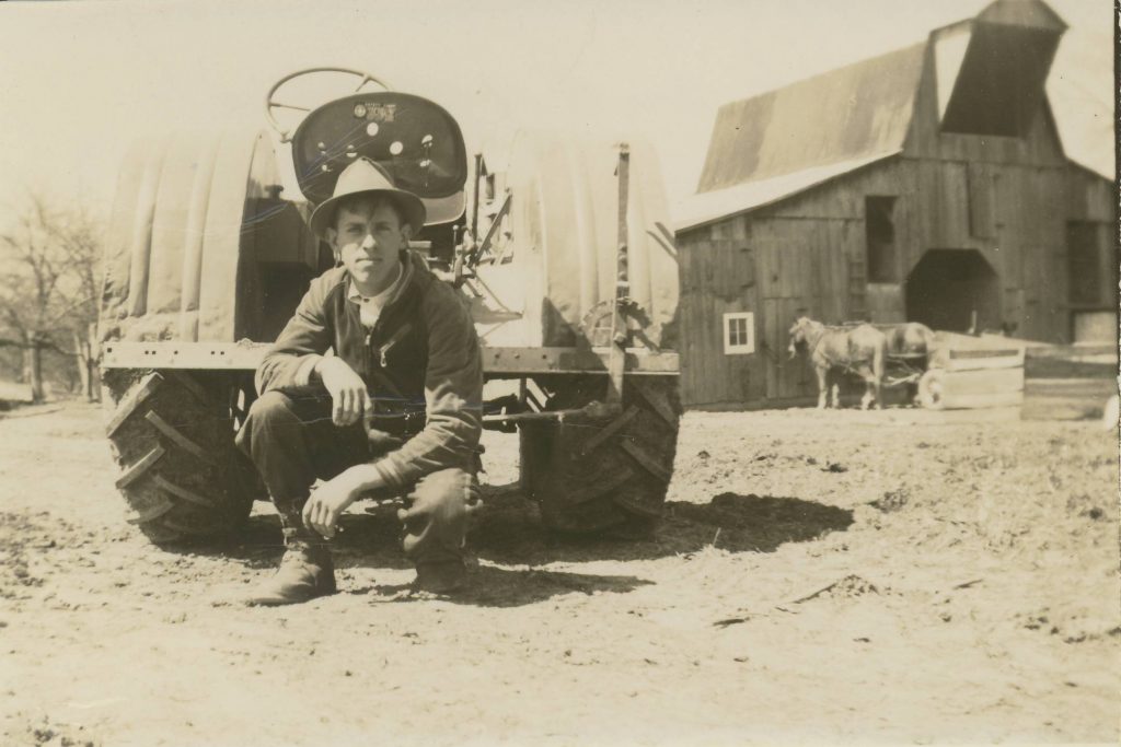 Black and white photograph of a man in front of an antique tractor