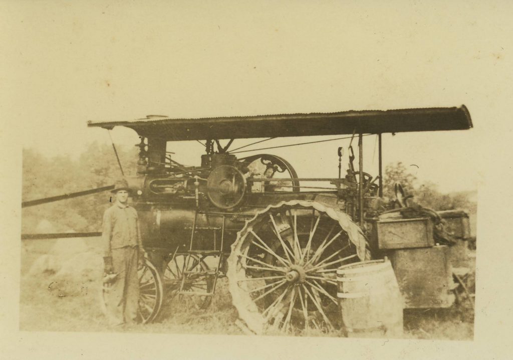 Black and white photograph of a man standing next to a steam engine tractor